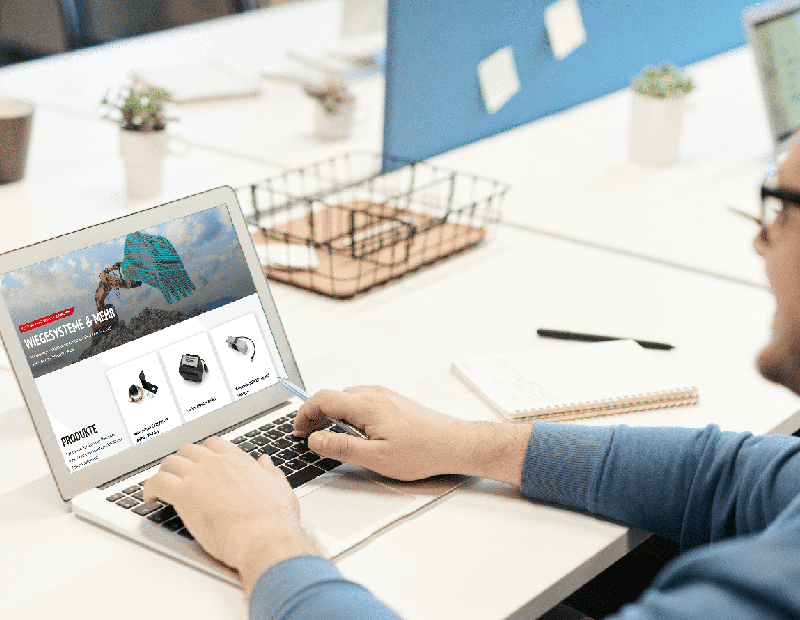 Person am Laptop betrachtet Pfreundt-Website für mobile Wiegesysteme, inklusive Bagger-, Band- und Radladerwaagen.