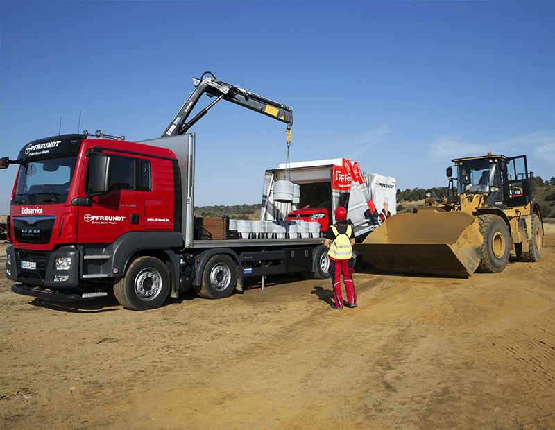 Lkw mit mobilen Pfreundt Wiegesystemen, Kran hebt Last. Radlader und Arbeiter vor blauem Himmel auf Baustelle.