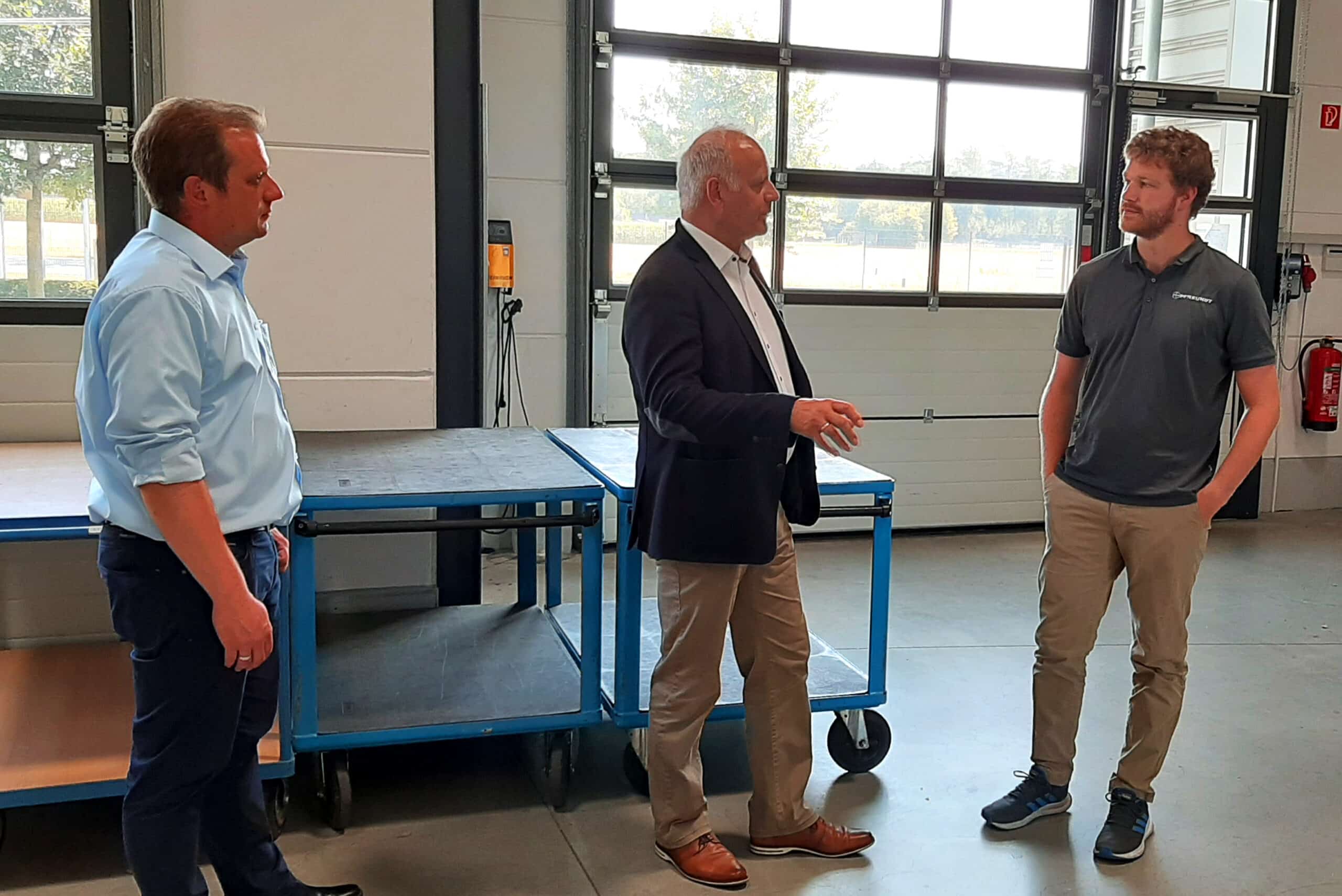 Drei Männer diskutieren in einer Werkshalle der Firma Pfreundt über mobile Wiegesysteme vor Werkbänken.