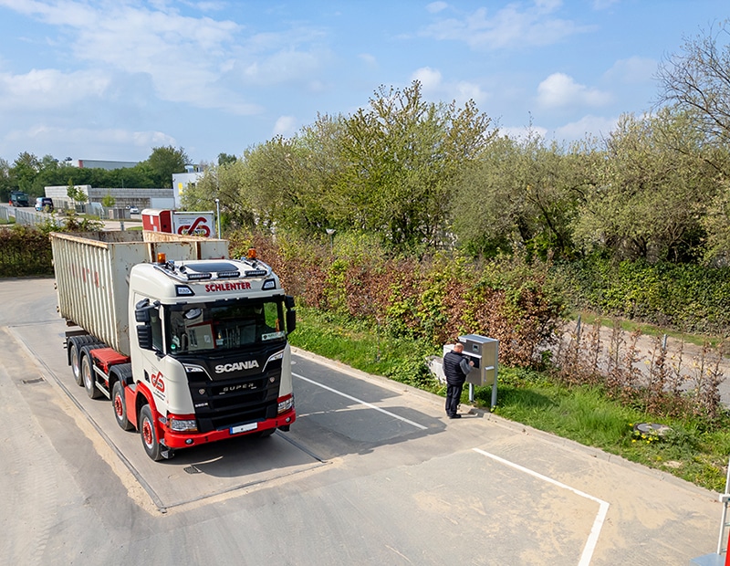 Lkw auf einer mobilen Wiegeplattform von Pfreundt, Fahrer interagiert mit Bedieneinheit, Frühlingsumgebung im Hintergrund.