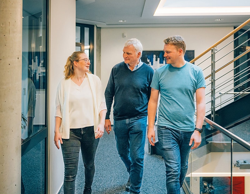 Drei Personen gehen lächelnd durch das Pfreundt-Büro, das mobile Wiegesysteme anbietet.