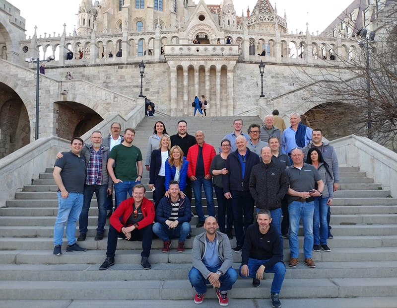 Gruppe von Pfreundt-Mitarbeitern auf einer Treppe vor historischer Architektur. Anbieter mobiler Wiegesysteme.