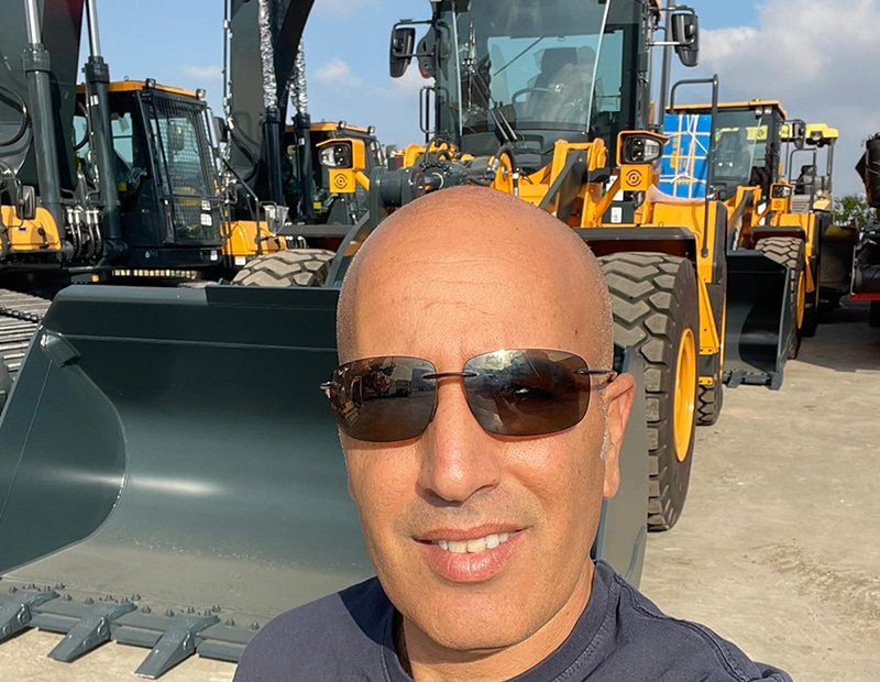 Mann mit Sonnenbrille vor gelben Baumaschinen, die mobile Wiegesysteme von Pfreundt nutzen.