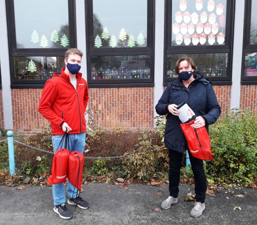 Zwei Personen mit Masken und roten Pfreundt-Taschen vor einem Gebäude mit weihnachtlicher Fensterdekoration.