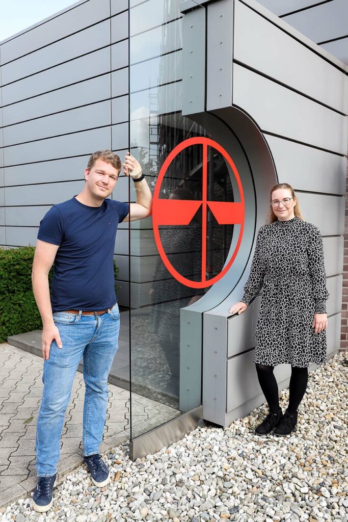 Zwei Personen vor dem Firmenlogo von Pfreundt, Anbieter von mobilen Wiegesystemen wie Bagger-, Band- und Kranwaagen.