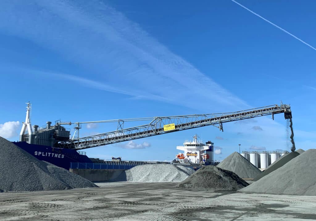 Förderband transportiert Schüttgut auf ein Schiff im Hafen, unterstützt durch Pfreundt Wiegesysteme für präzise Messungen.