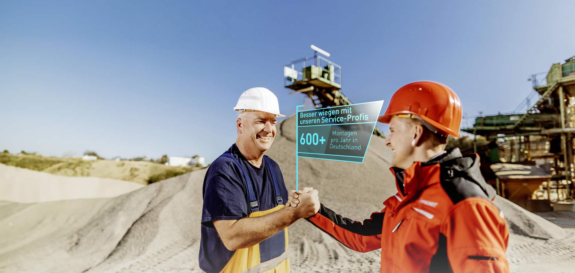 Zwei Männer in Schutzhelmen schütteln Hände vor einer industriellen Kulisse. Textbox: 600+ Montagen pro Jahr in Deutschland.