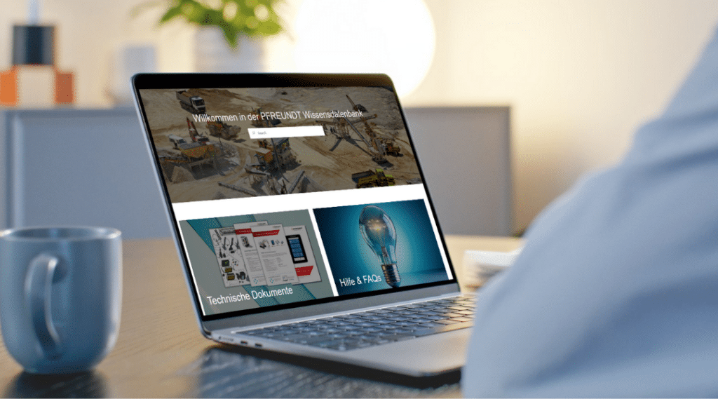 Laptop mit Pfreundt-Webseite, die mobile Wiegesysteme und technische Dokumente zeigt; daneben eine Tasse.