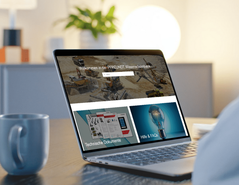 Laptop mit Pfreundt Wissensdatenbank, zeigt technische Dokumente und FAQs, bei Tisch mit Tasse.