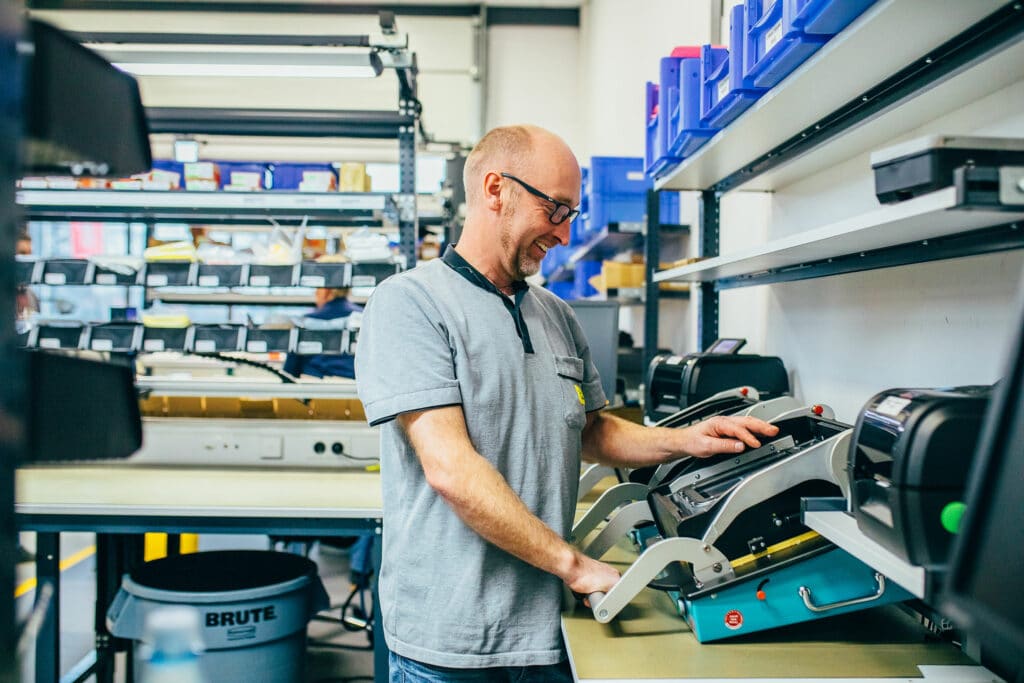 Mitarbeiter montiert mobile Wiegesysteme bei Pfreundt in einem Lager mit Regalen voller Geräte und Zubehör.