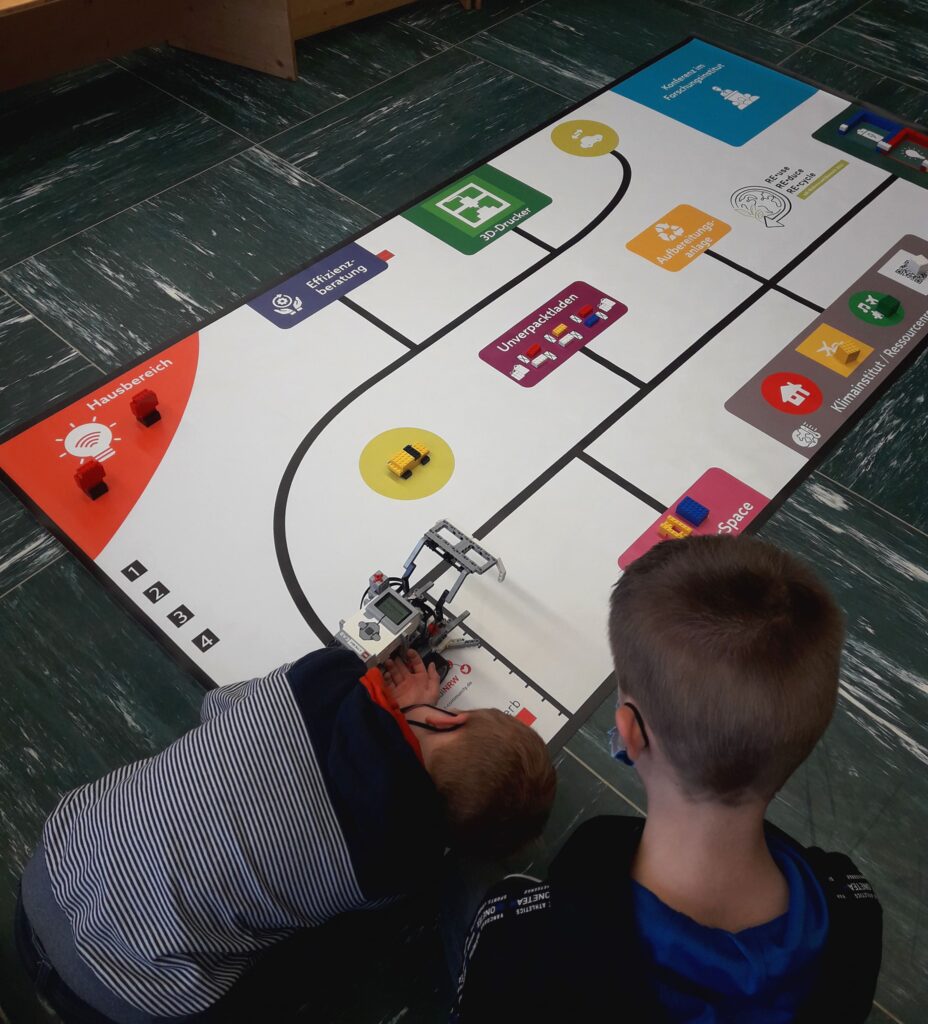 Kinder programmieren Roboter auf einem Spielfeld. Pfreundt bietet innovative mobile Wiegesysteme für diverse Anwendungen an.