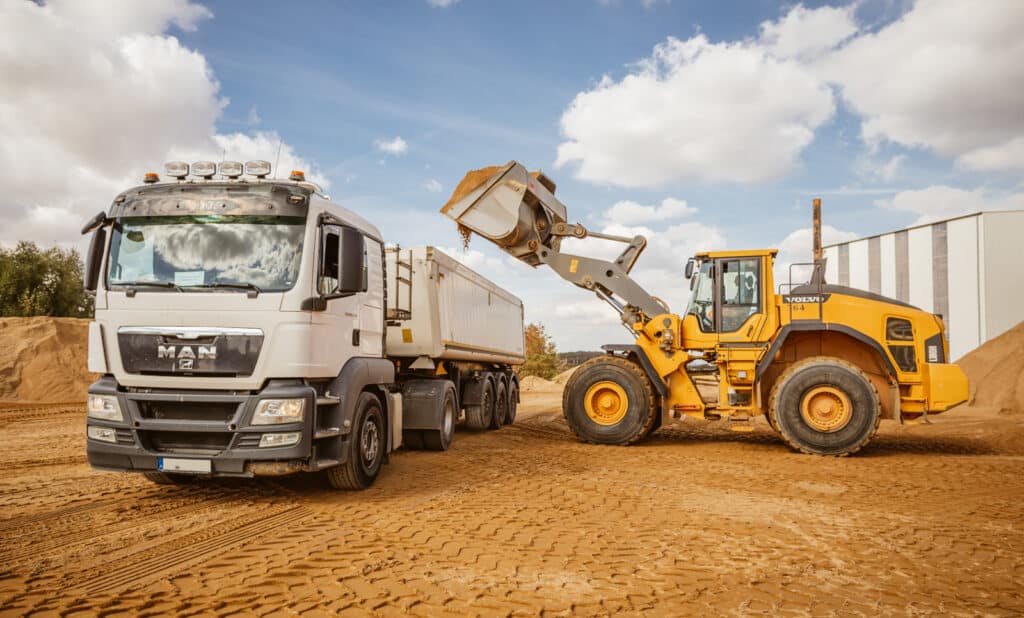 Bagger lädt Sand auf LKW, demonstriert Pfreundts mobile Wiegesysteme für effiziente Baulösungen.