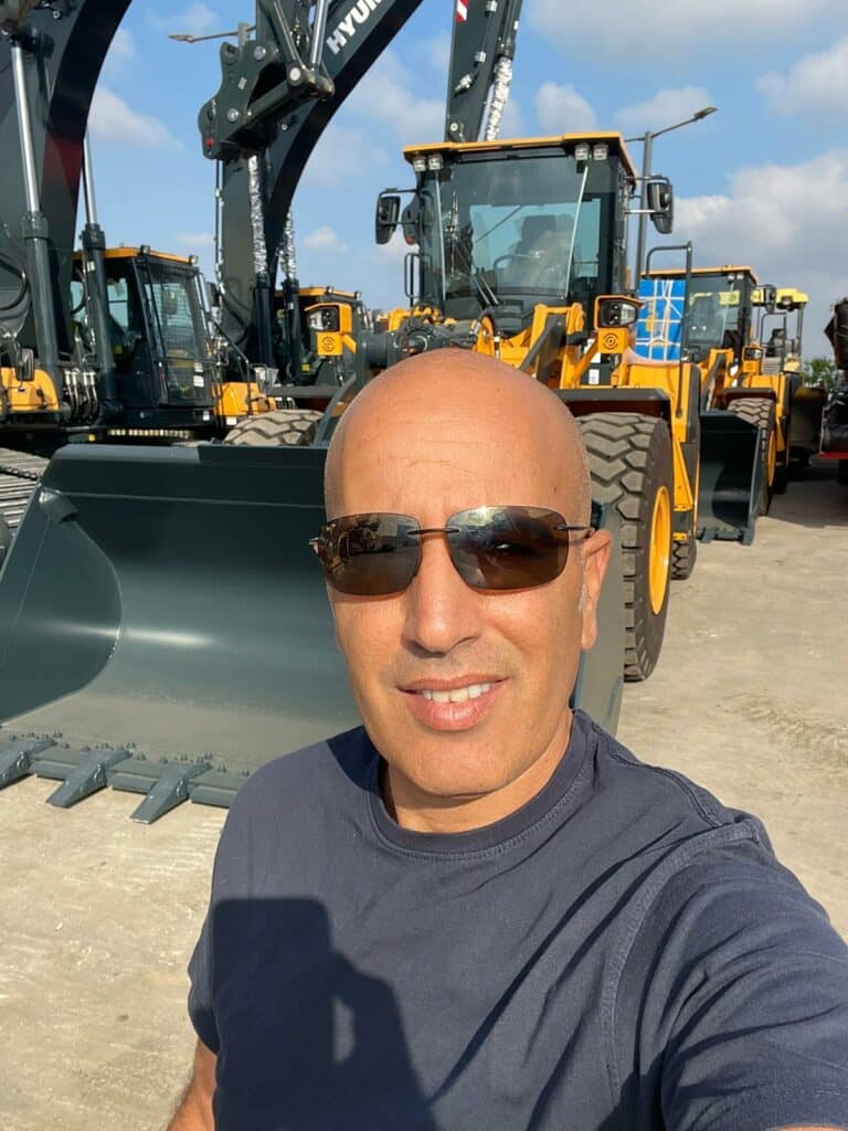 Person mit Sonnenbrille vor gelben Baumaschinen, präsentiert Pfreundt mobile Wiegesysteme.