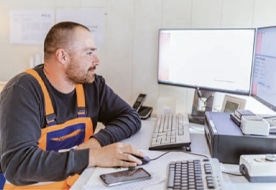 Mitarbeiter in Arbeitskleidung am Computer, analysiert Daten für Pfreundt mobile Wiegesysteme wie Bagger- und Kranwaagen.