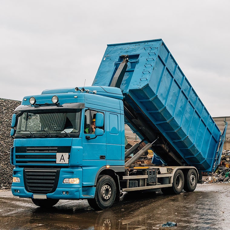 Blauer Kipp-LKW mit aufgerichteter Ladefläche auf Industriehof, Pfreundt mobile Wiegesysteme im Einsatz.
