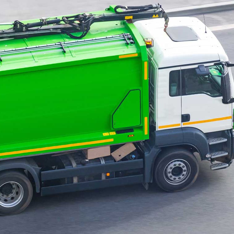 Grüner Müllwagen auf einer Straße, dargestellt für mobile Wiegesysteme von Pfreundt.