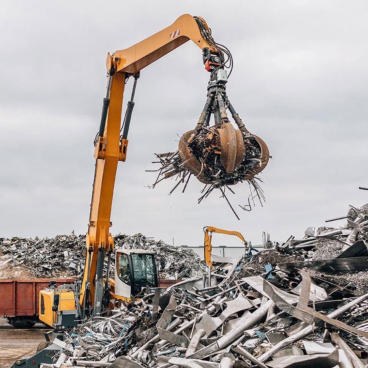 Bagger hebt Schrott mit Greifer bei Einsatz von Pfreundts mobilem Wiegesystem auf Recyclingplatz.