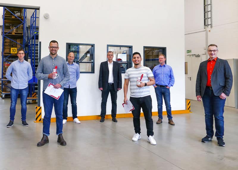 Gruppe von Pfreundt-Mitarbeitern in der Produktionshalle, lächelnd mit Zertifikaten. Anbieter mobiler Wiegesysteme.