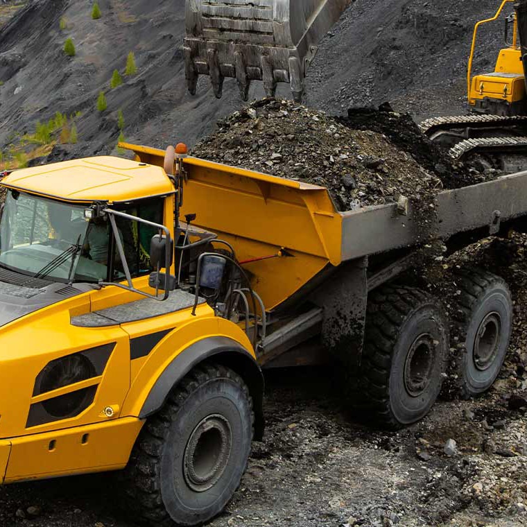 Gelber Bagger lädt Schutt auf Lastwagen in Steinbruch. Pfreundt bietet mobile Wiegesysteme für Bau- und Industriefahrzeuge.