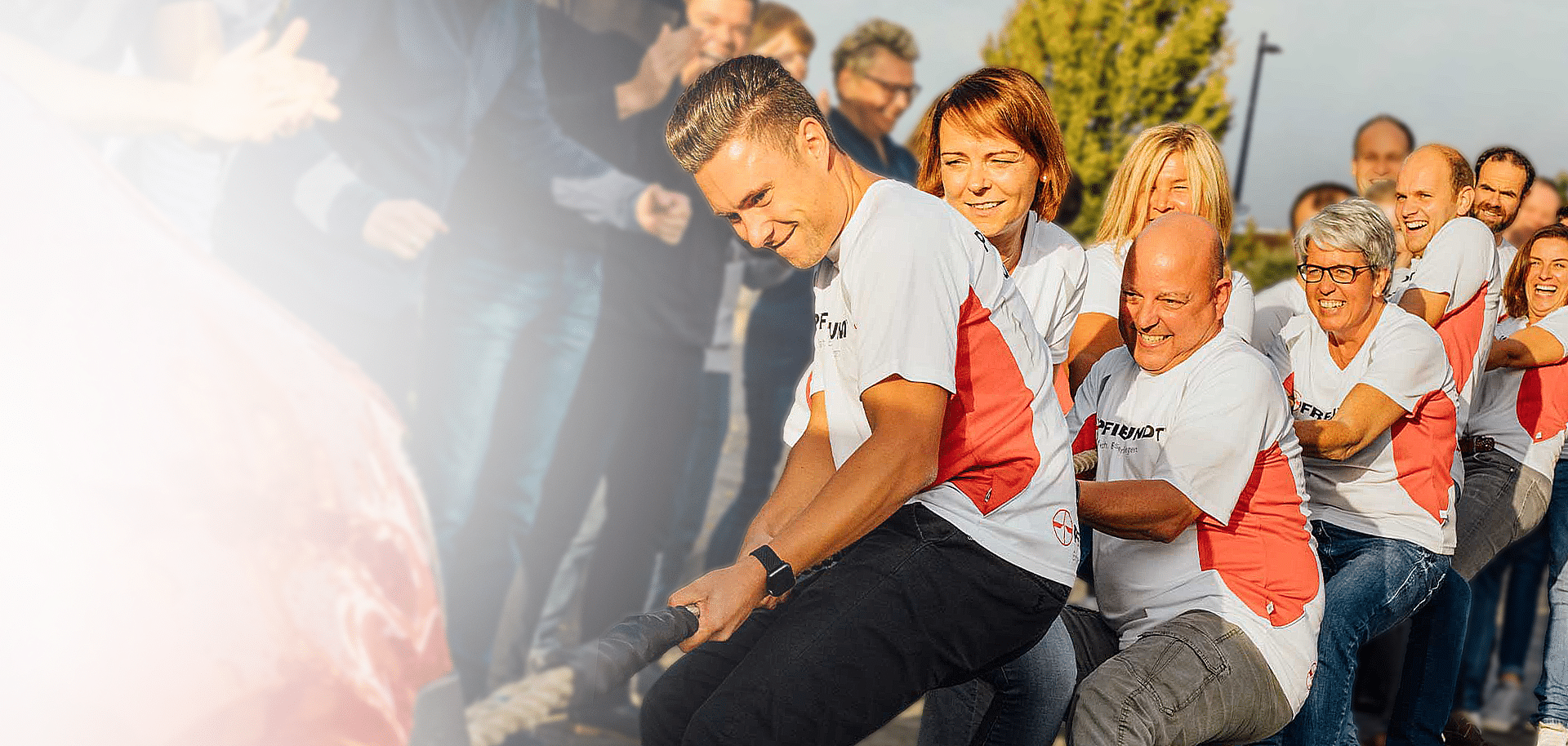 Eine Gruppe von Menschen bei einem Tauziehen-Event, lachend, in Pfreundt-Shirts.