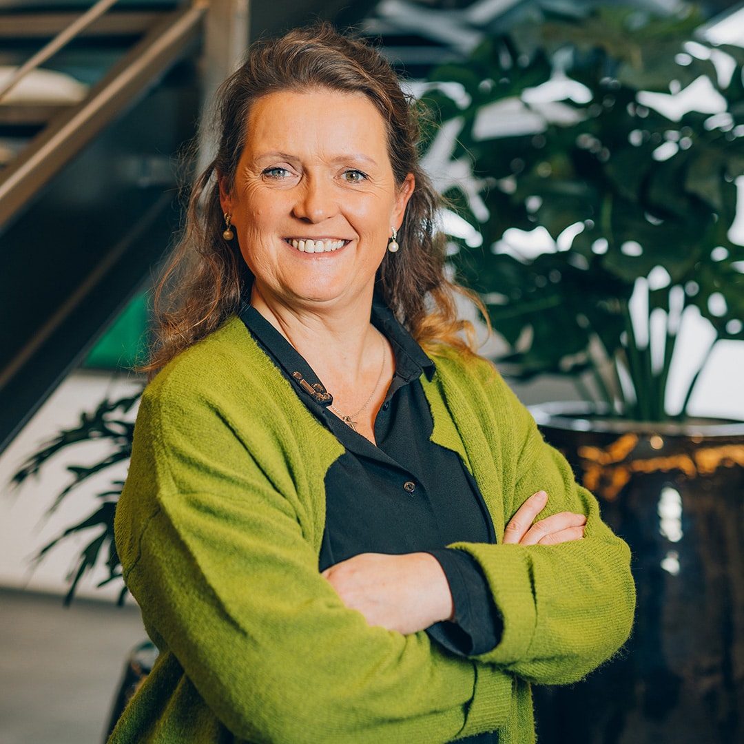 Eine Frau in grüner Jacke lächelt, Pfreundt-Logo und Pflanzen im Hintergrund. Mobile Wiegesysteme im Fokus.