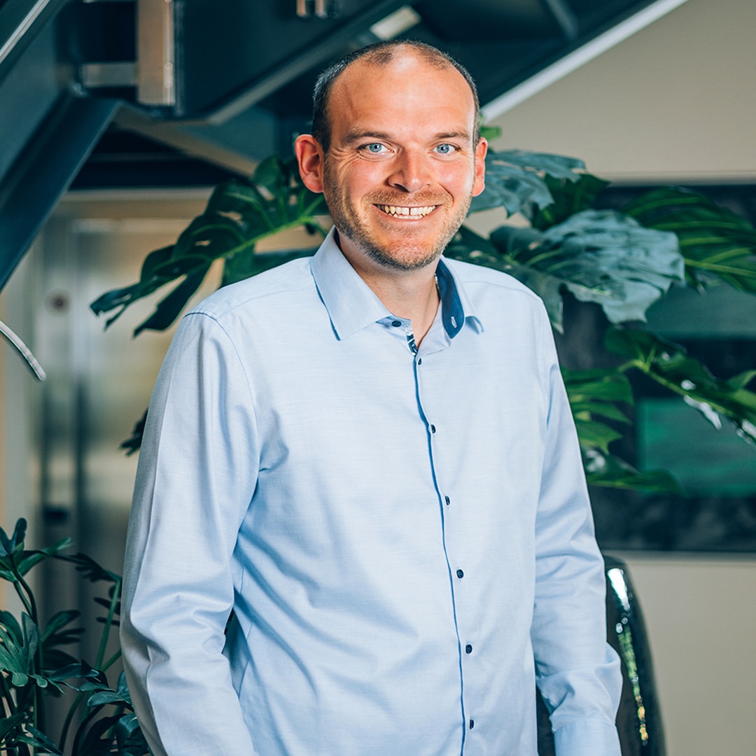 Person in hellem Hemd lächelnd vor Pflanzen im Büro von Pfreundt, Anbieter mobiler Wiegesysteme.