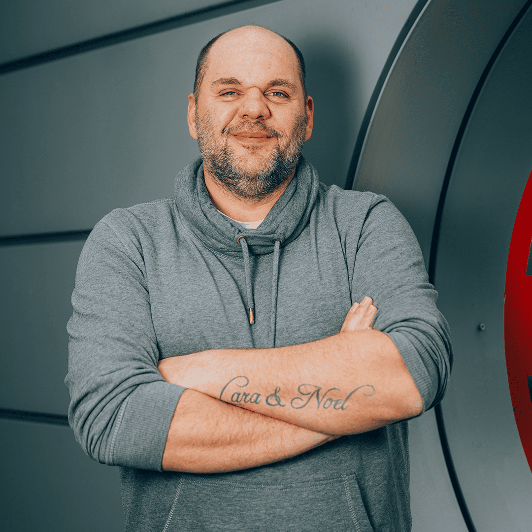 Eine Person in grauem Hoodie posiert vor einer Wand bei Pfreundt, spezialisiert auf mobile Wiegesysteme.