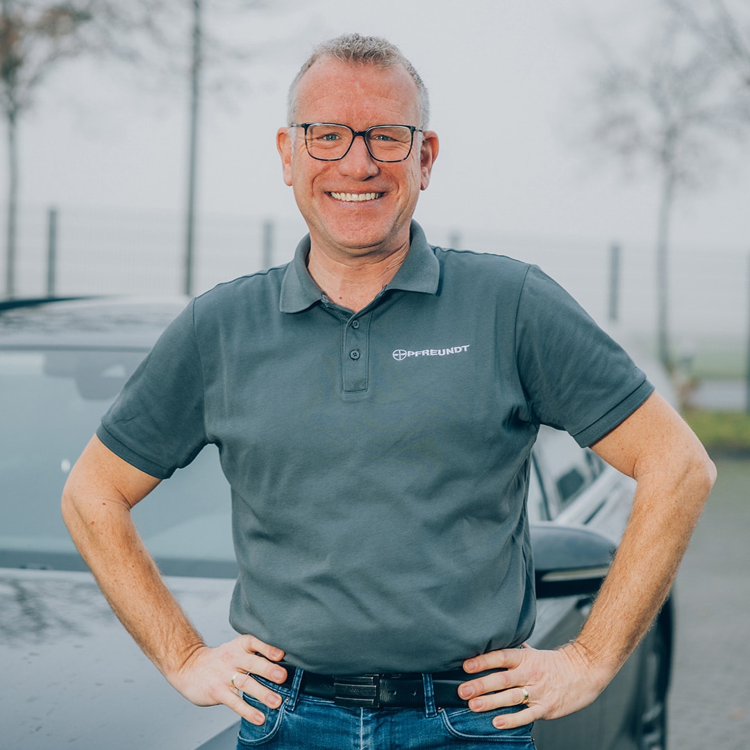 Mann im Pfreundt-Shirt vor einem Auto, draußen. Pfreundt bietet diverse mobile Wiegesysteme an.