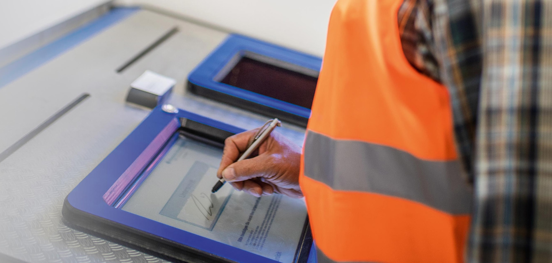 Person signiert auf einem digitalen Bildschirm in einer industriellen Umgebung.
