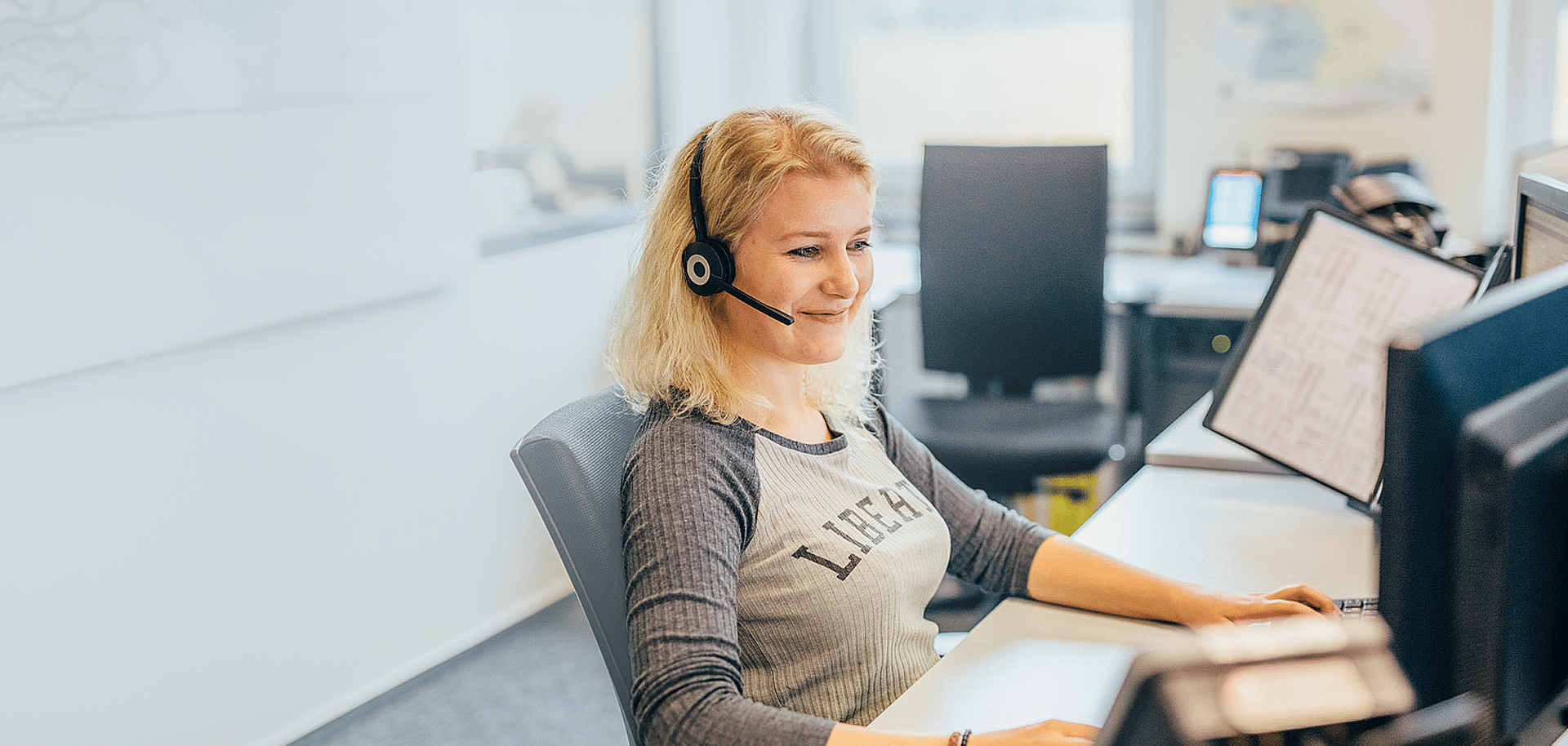 Frau im Büro telefoniert mit Headset, arbeitet am Computer bei Pfreundt, Anbieter von mobilen Wiegesystemen.
